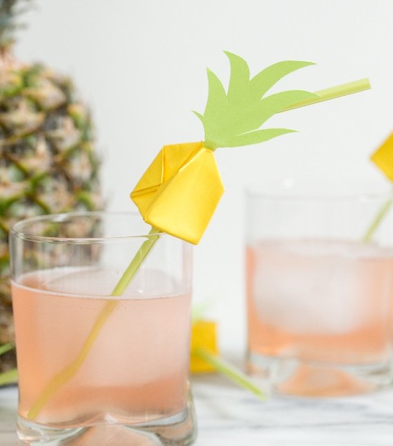 Pineapple Origami on a straw in a glass of juice. Pineapple behind